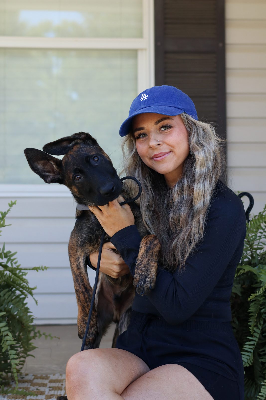 A woman in a blue cap holding a brindle puppy on a porch