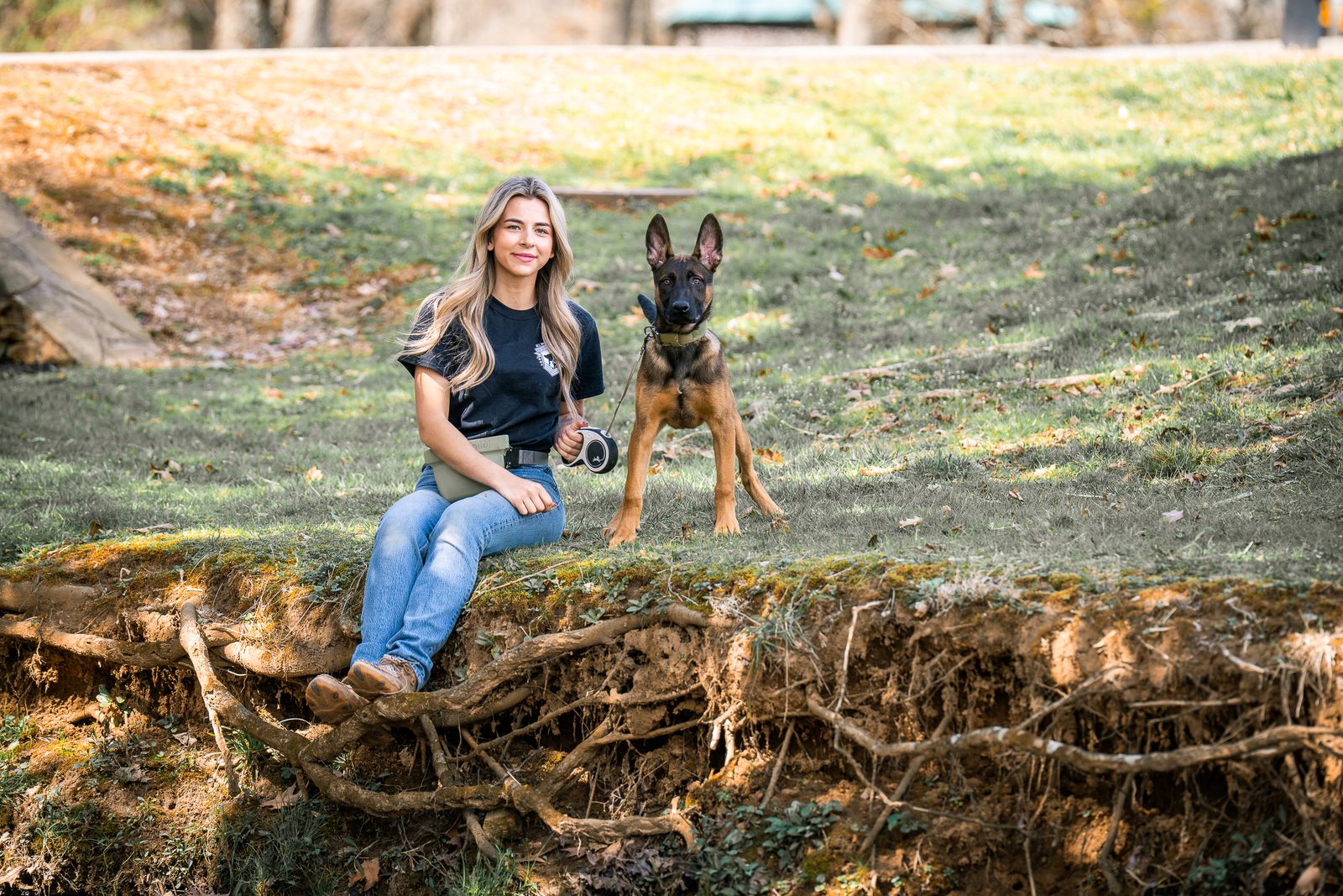 A woman sitting on a mossy bank with a young dog beside her