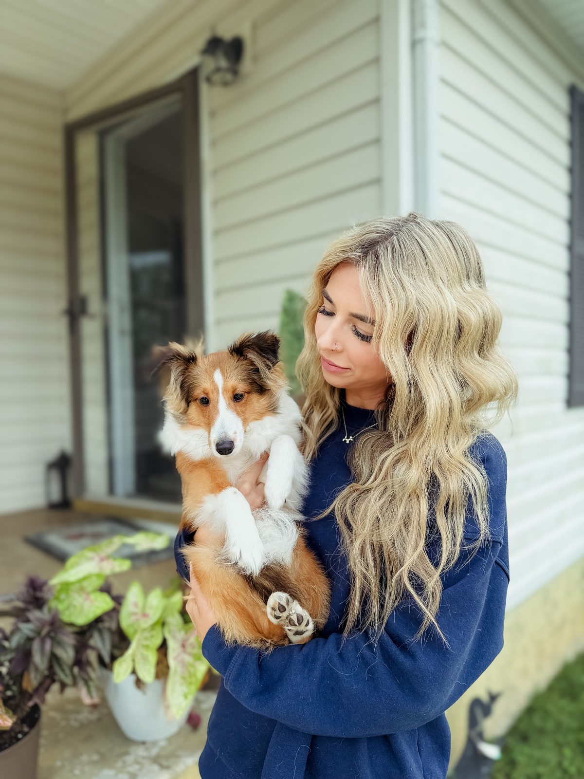 A woman cradling a sheltie puppy on a front porch